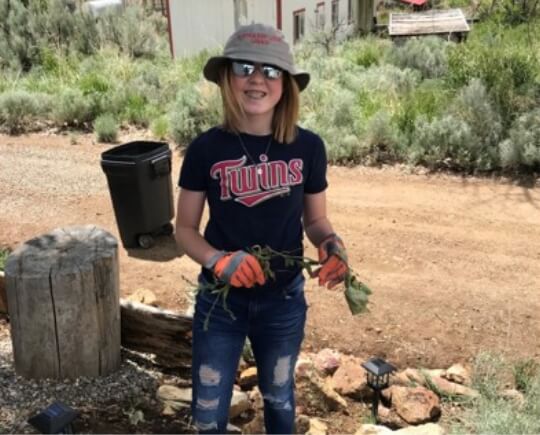 A young girl with a plant in her hand smiling.