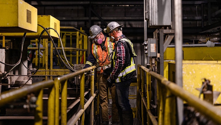 Two men working on huge machinery wearing heavy duty face masks